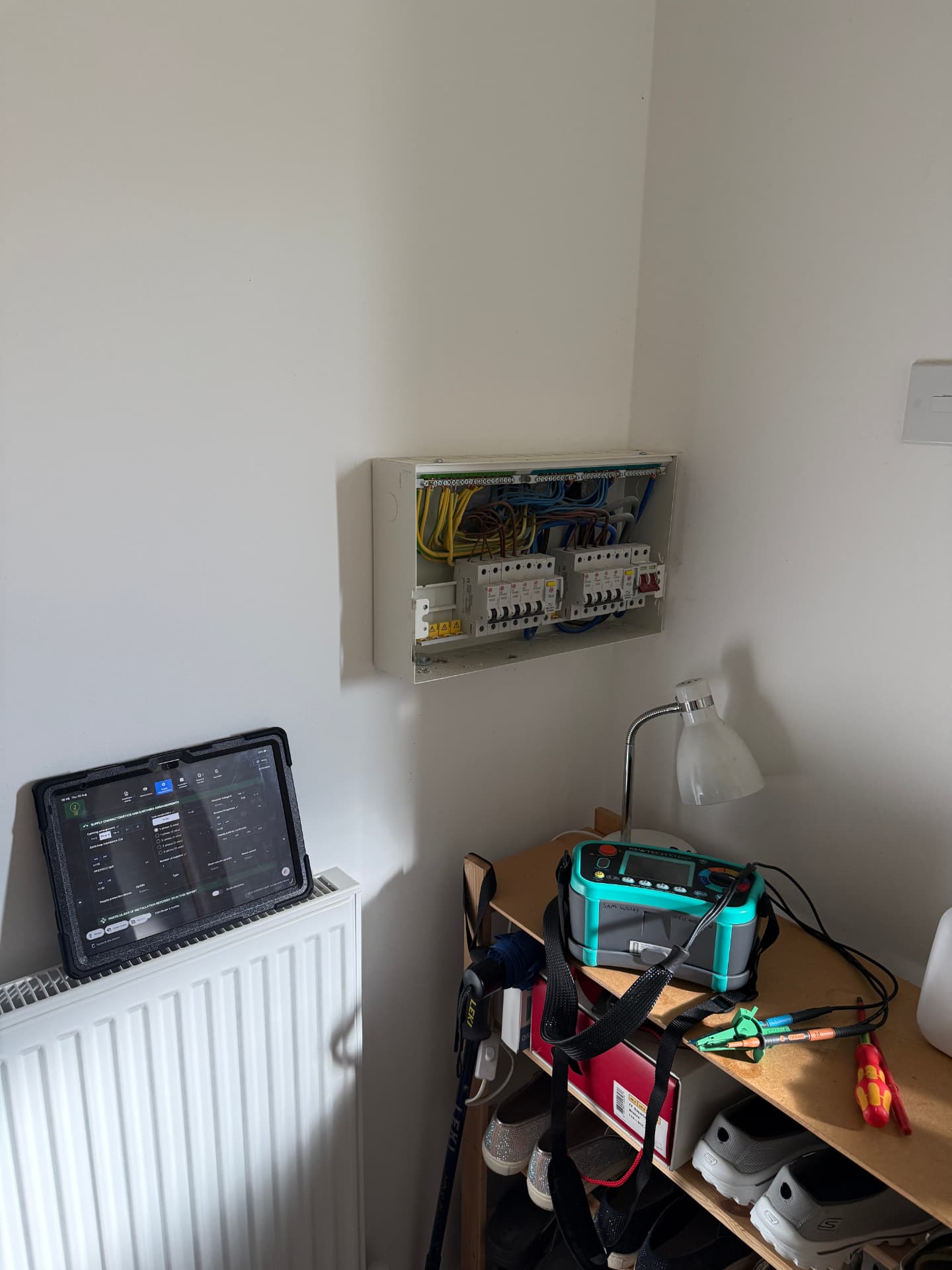 EICR inspection in progress with consumer unit cover removed and test results recorded on a tablet